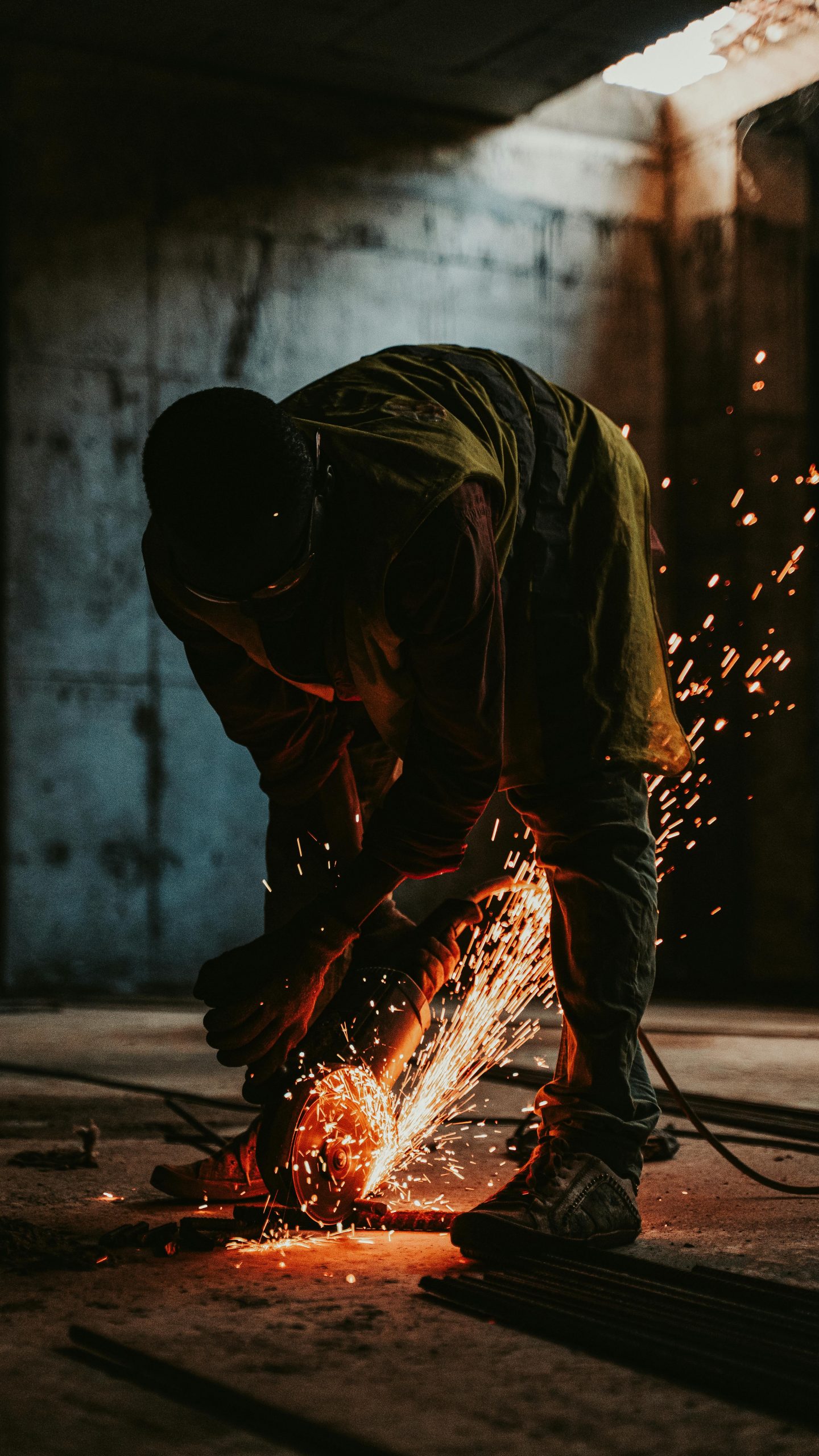 Worker in silhouette cutting metal with sparks in a construction site at sunset.